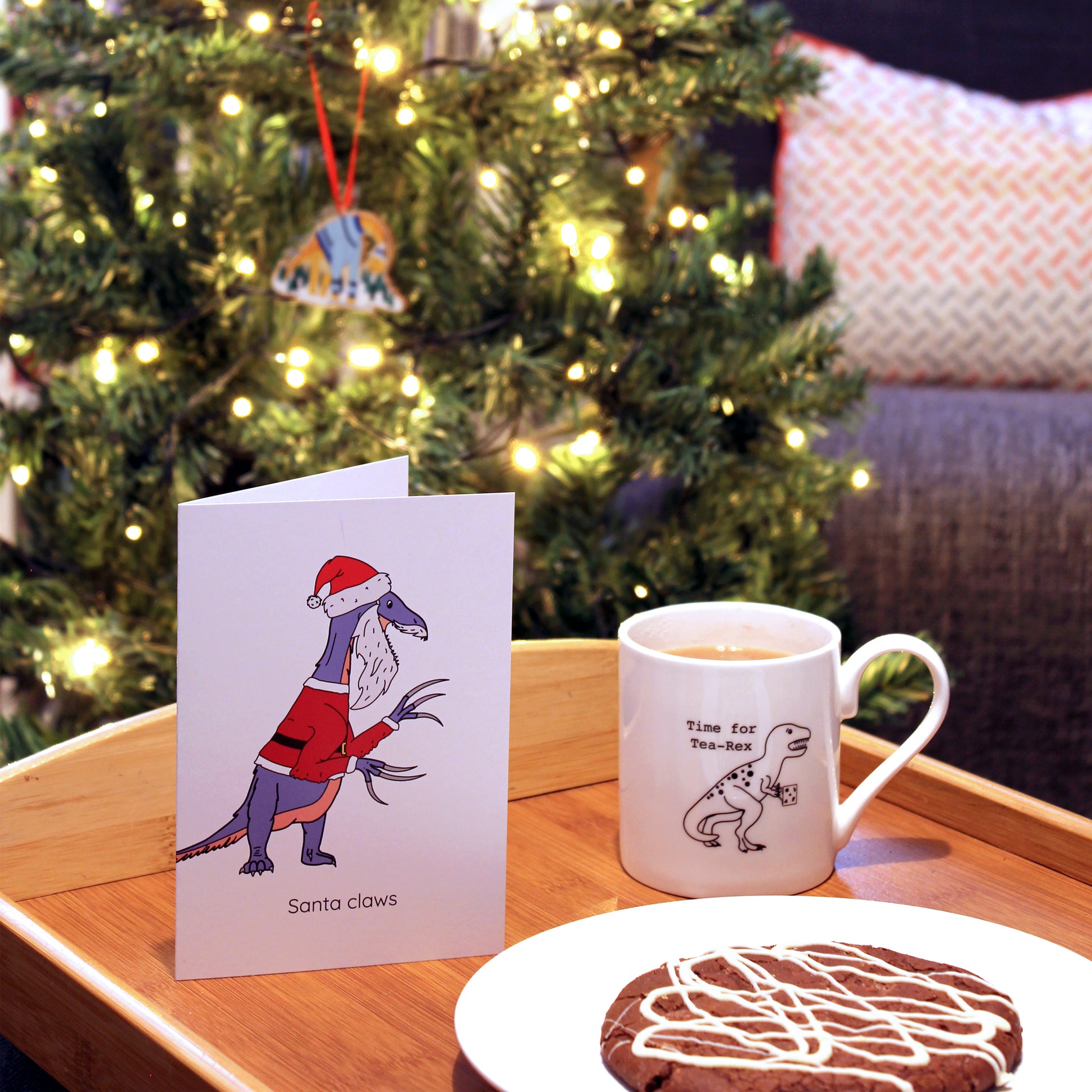 Santa claws greeting card on a tray with a cookie and a cup of tea, there is a Christmas tree in the background