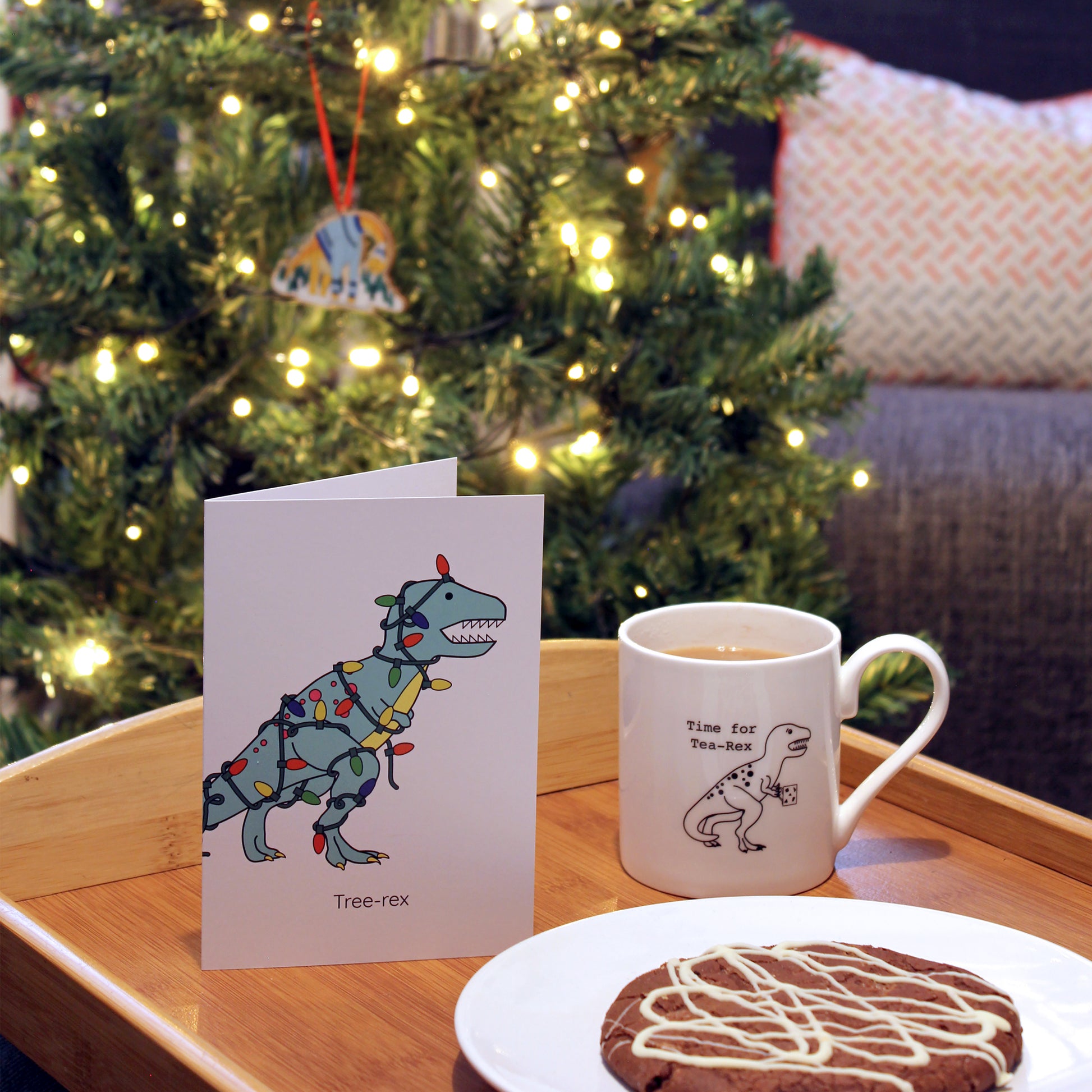 tree-rex greeting card on a tray with a cookie and a cup of tea, there is a Christmas tree in the background