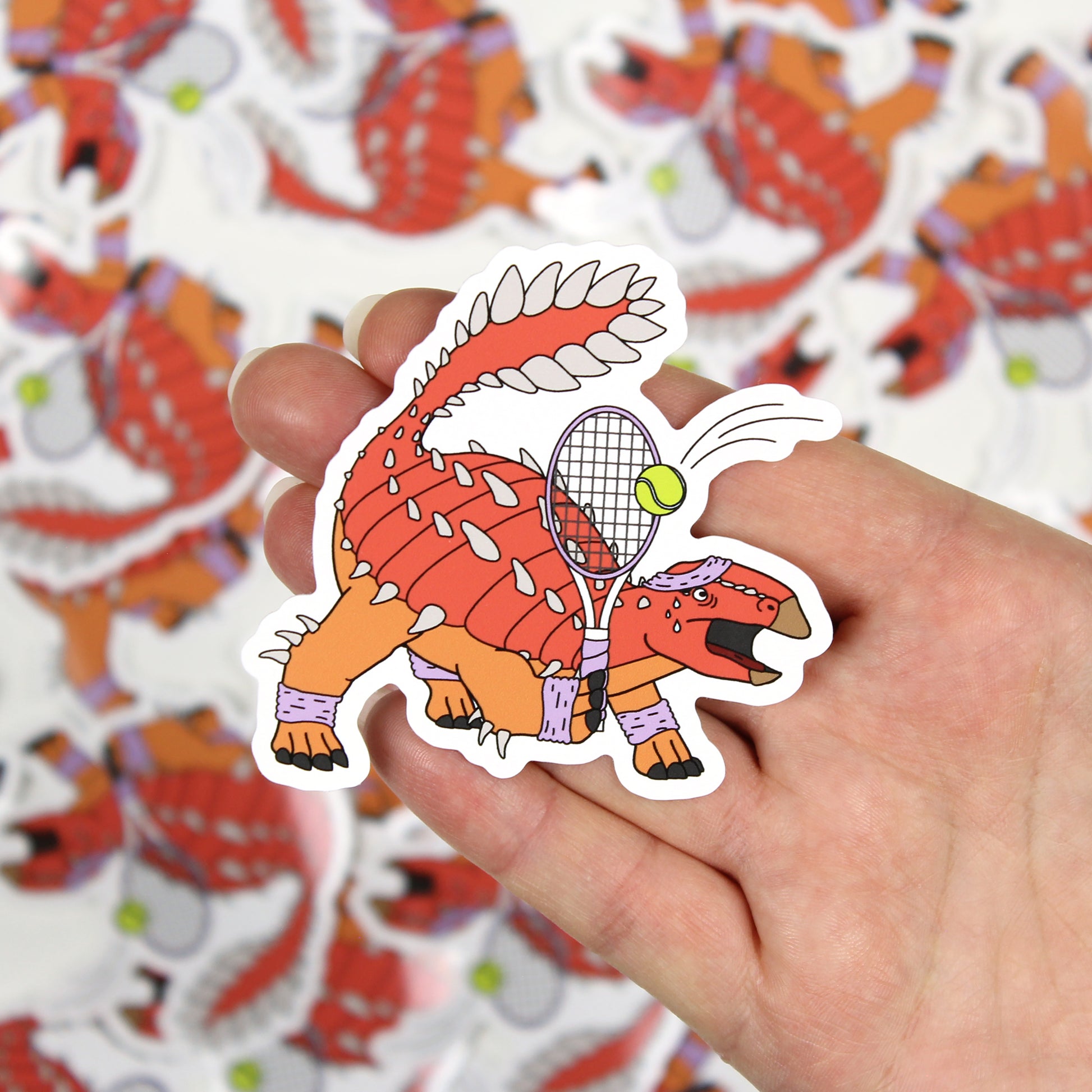 Tennis dinosaur sticker on a hand with out of focus stickers in the background.