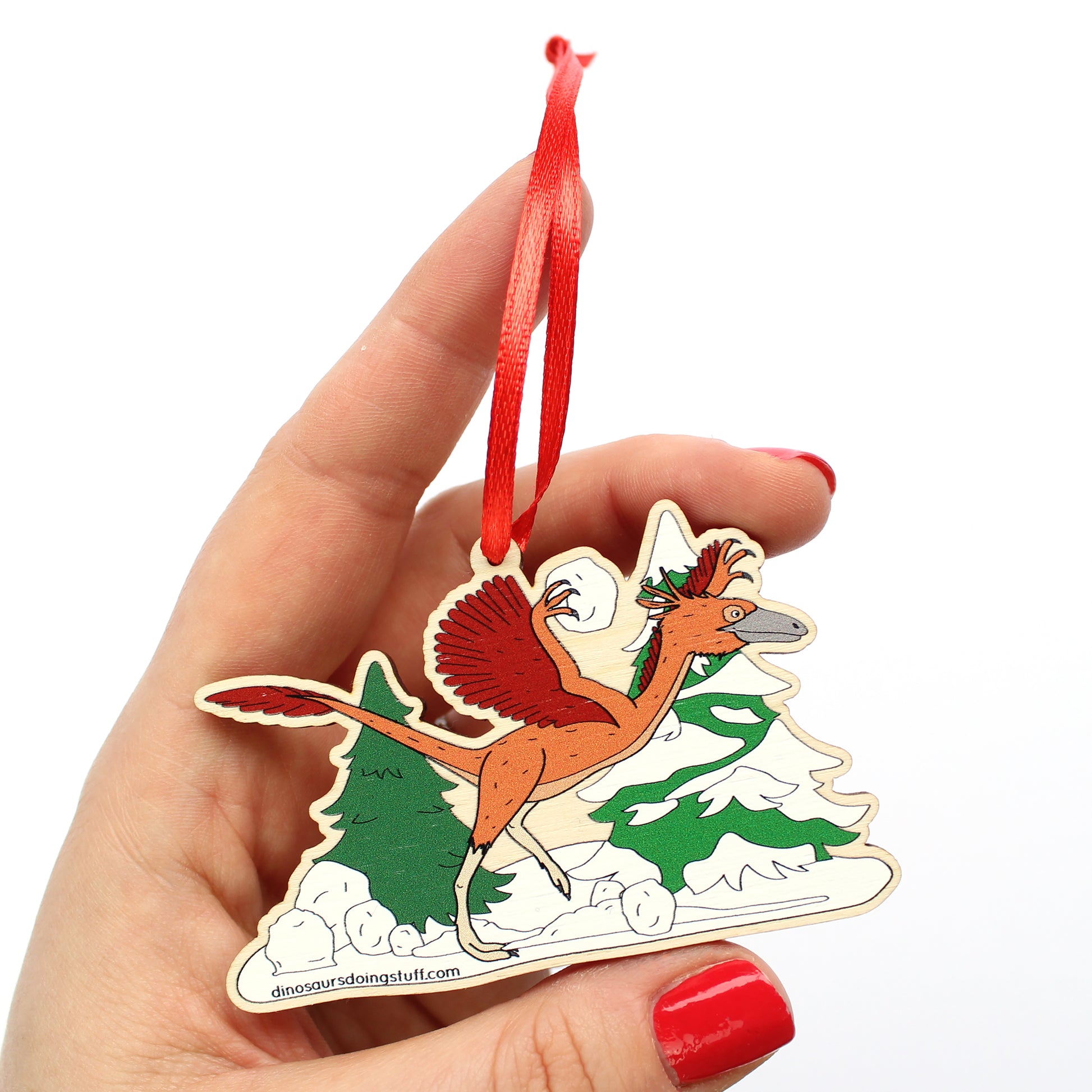 Hand holding a wooden Christmas decoration featuring a dinosaur throwing snowballs