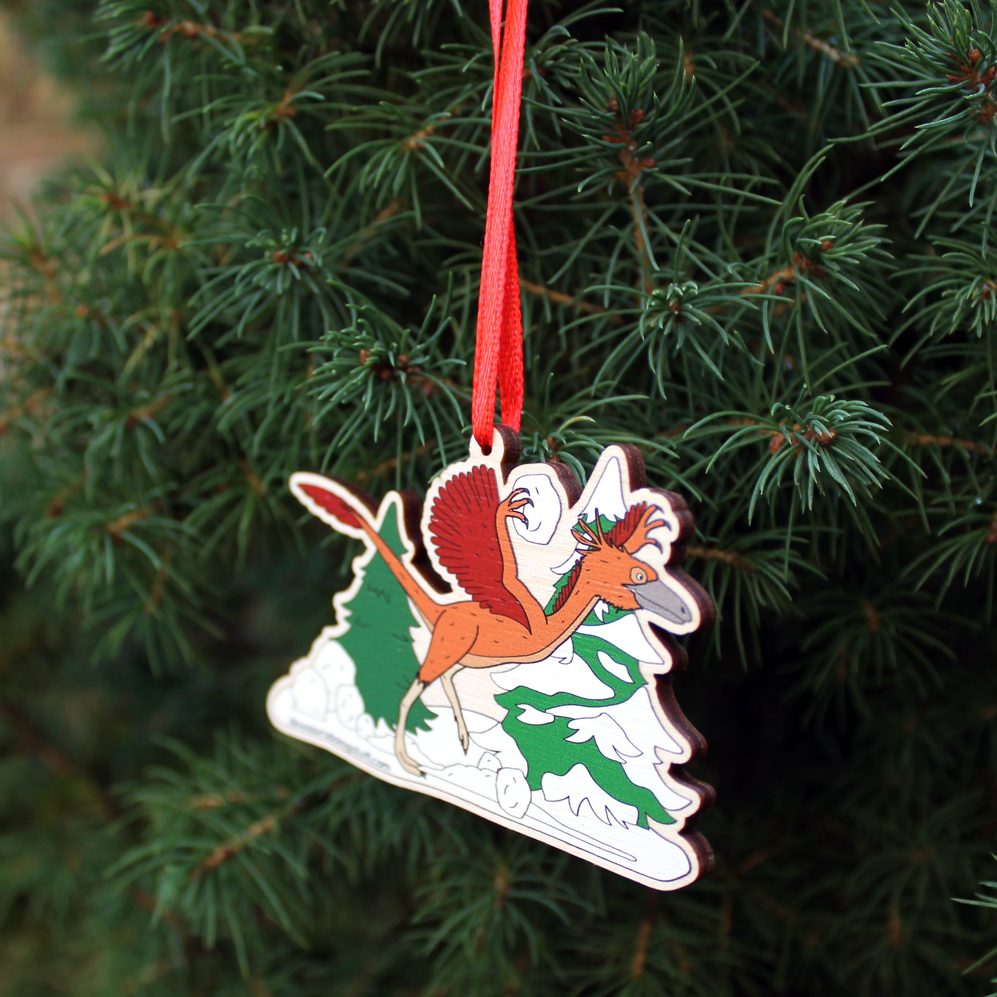 wooden Christmas decoration featuring a dinosaur throwing snowballs hanging on a Christmas Tree