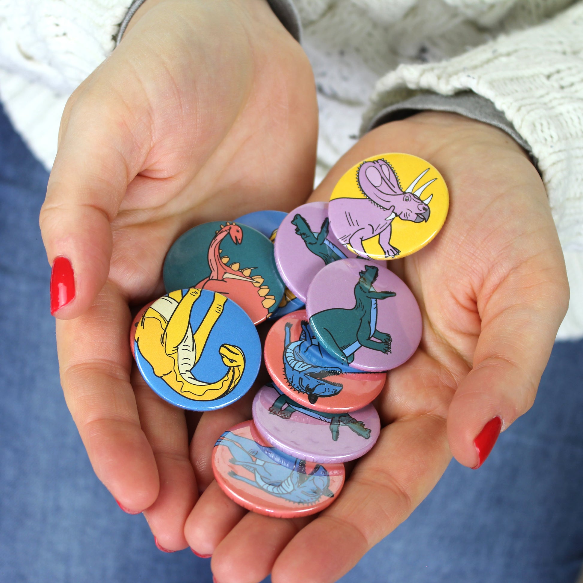 hands holding a pile of mini dinosaur badges