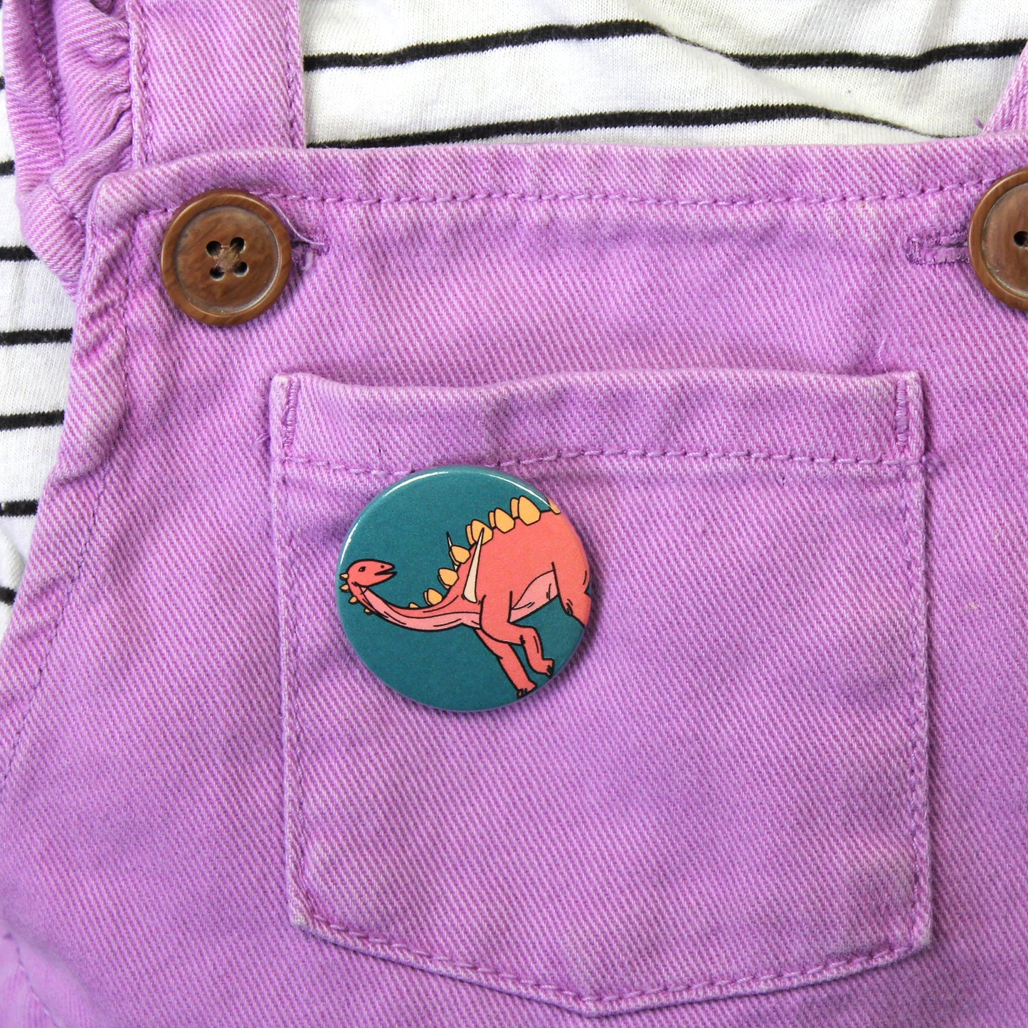 green Miragaia badge on a purple kids dungaree dress