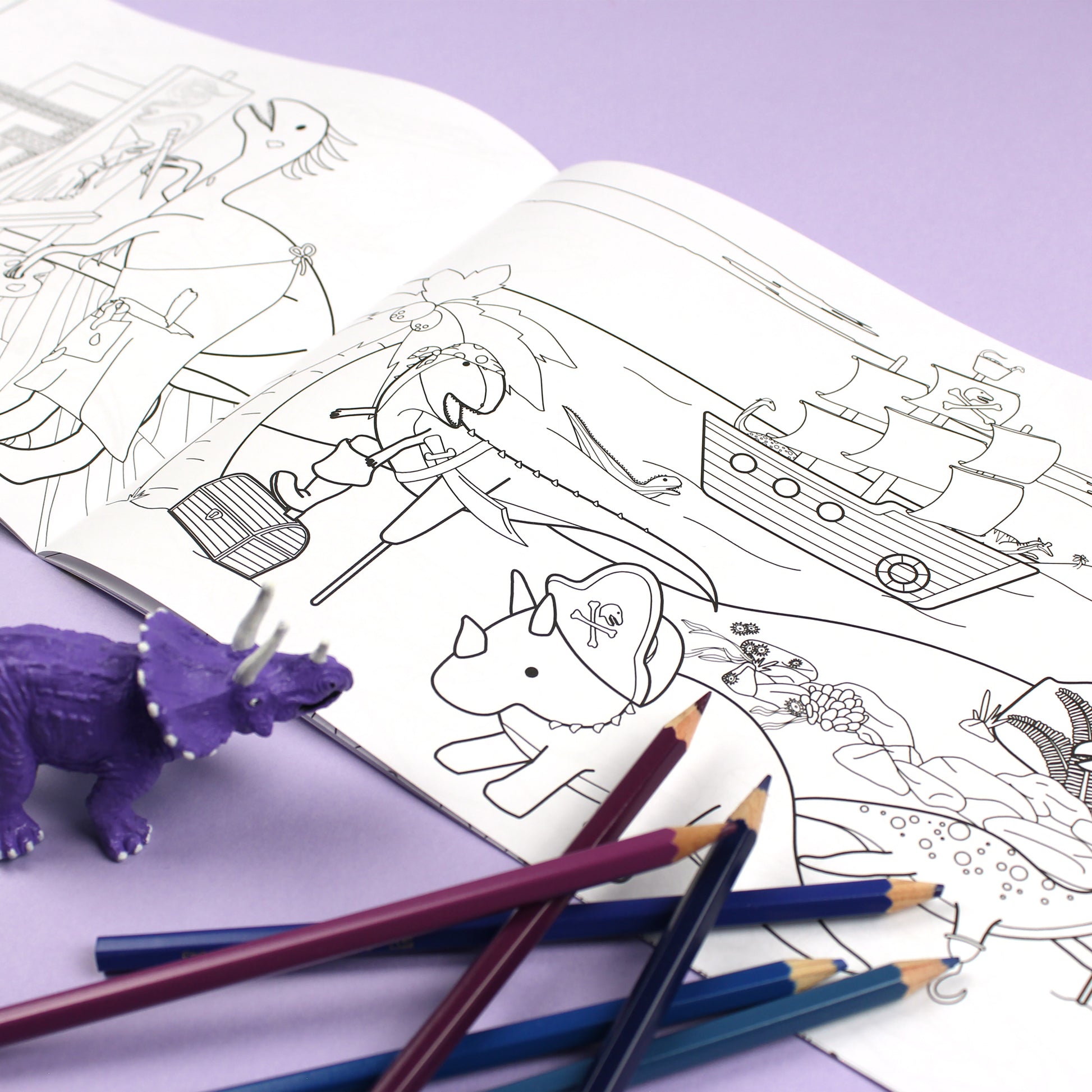 Inside page of Dinosaurs Doing Stuff colouring book. The page features black line illustrations of dinosaurs dressed as pirates on a beach, there is a pirate ship in the ocean.