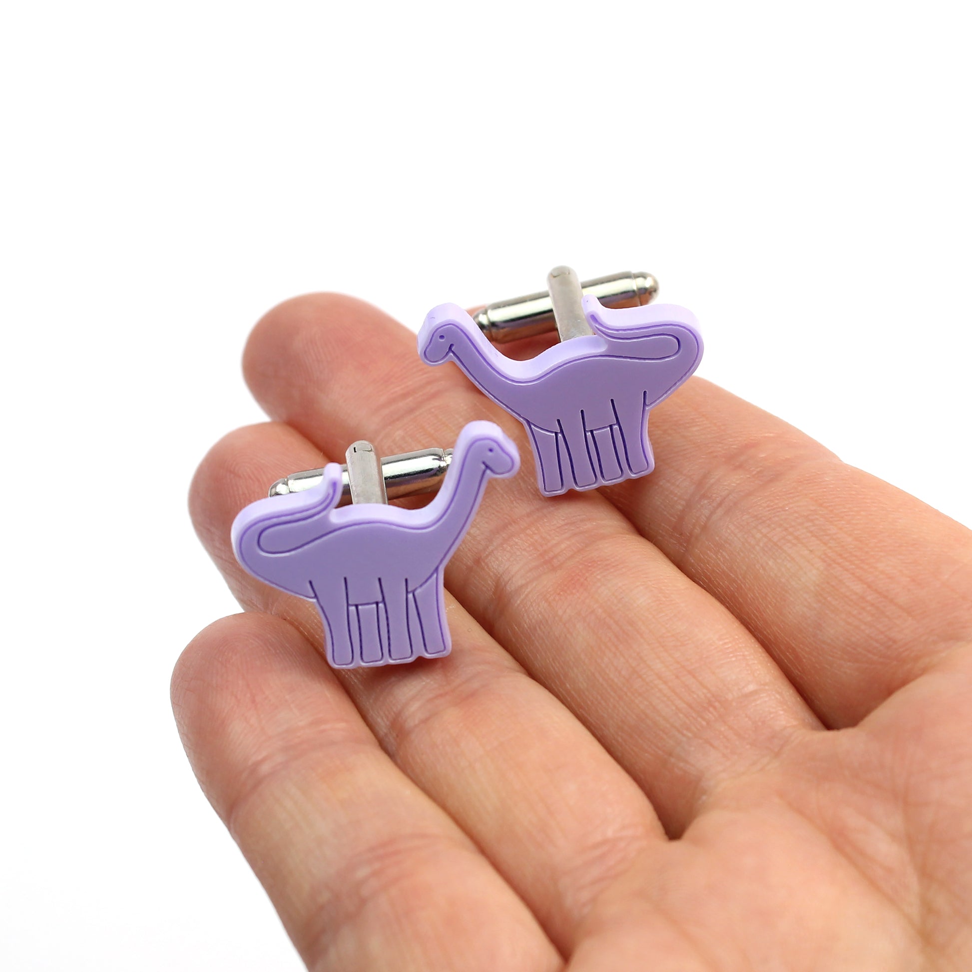 a pair of purple brontosaurus cufflinks sitting on a hand