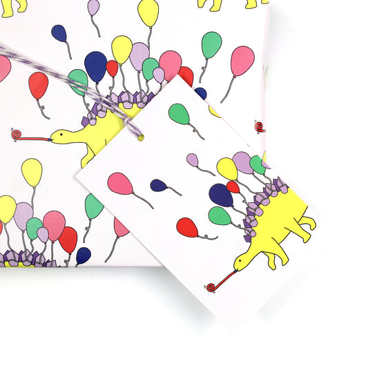 dinosaur stegosaurus party animal gift tag sitting on a box covered with matching wrapping paper