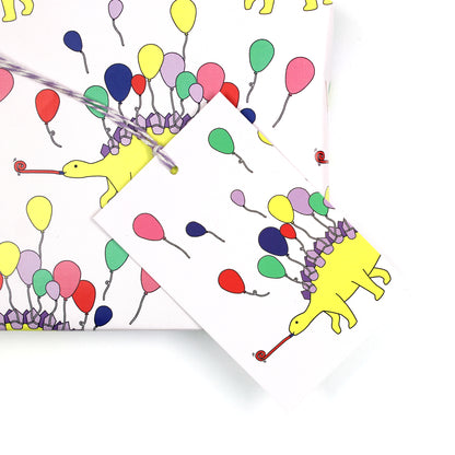 dinosaur stegosaurus party animal gift tag sitting on a box covered with matching wrapping paper