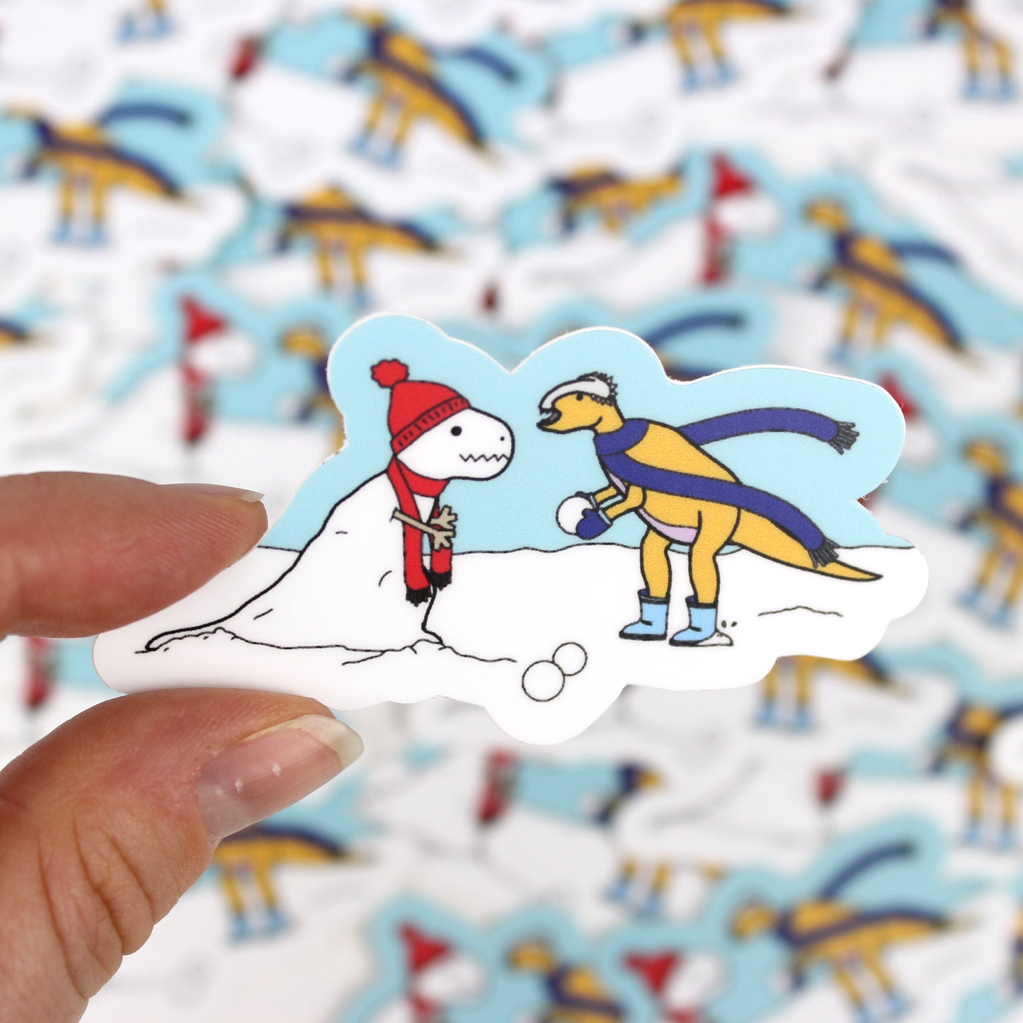 dinosaur making a snow-rex snow man sticker held by a hand