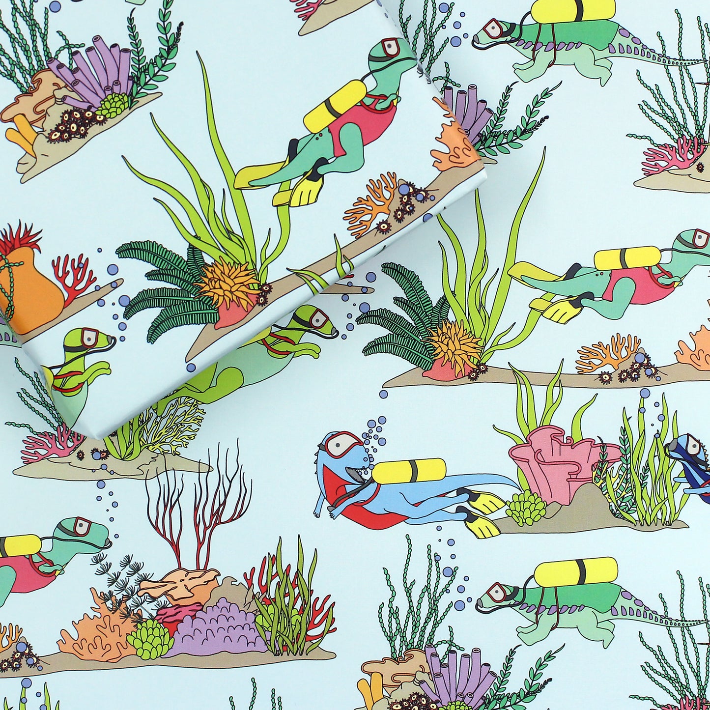 a sheet of Under the Sea Dinosaur Wrapping Paper with a box on top that is also wrapped in the same paper