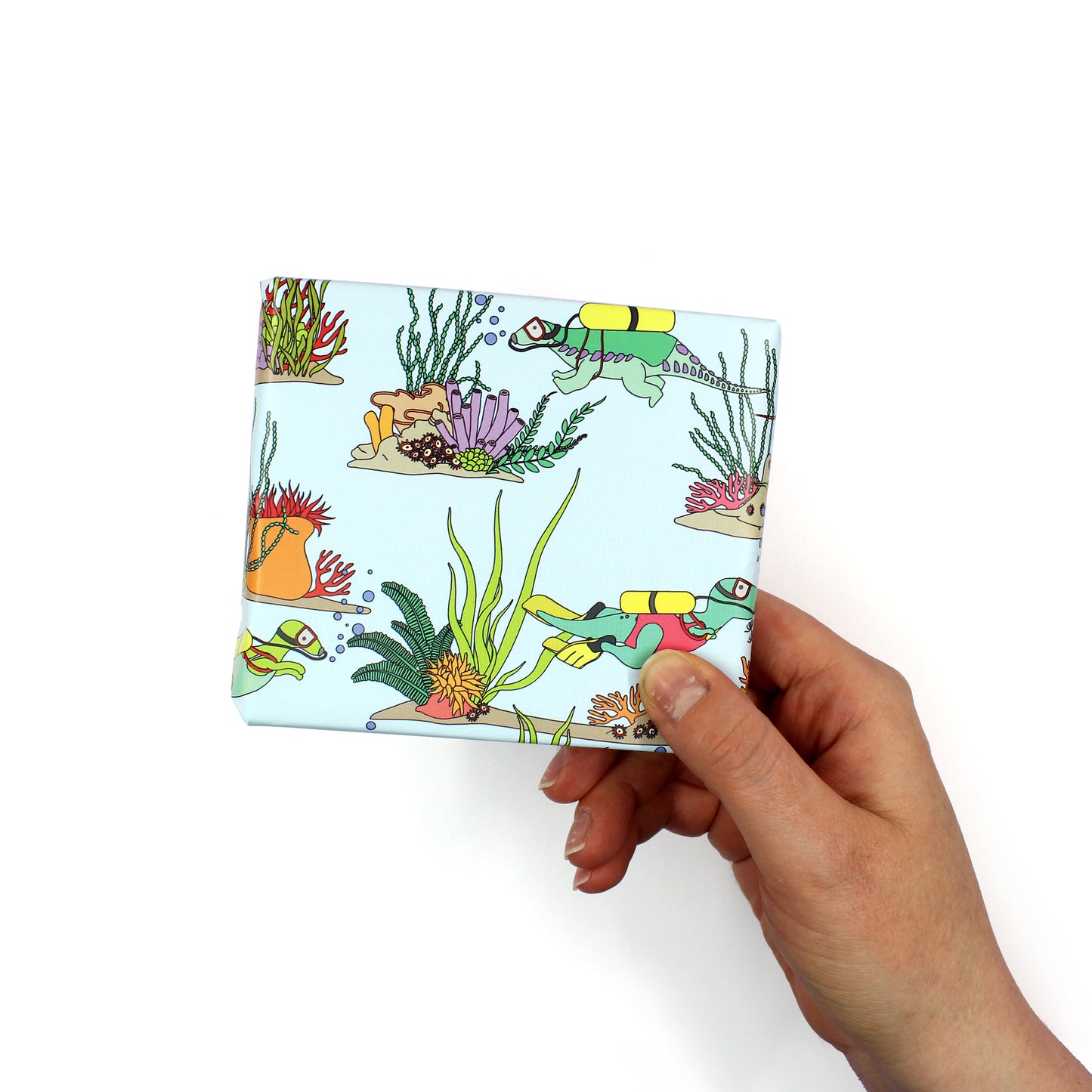 a hand holding a small box that is wrapped in Under the Sea Dinosaur Wrapping Paper