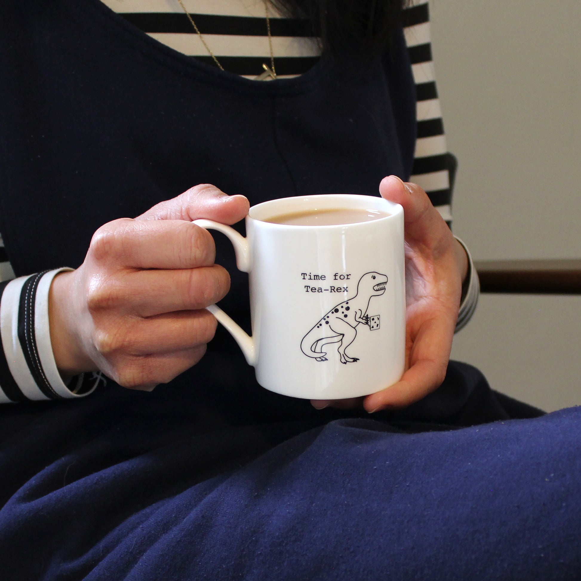 Time for Tea-Rex Mug held by a person in a navy jumpsuit and stripe top