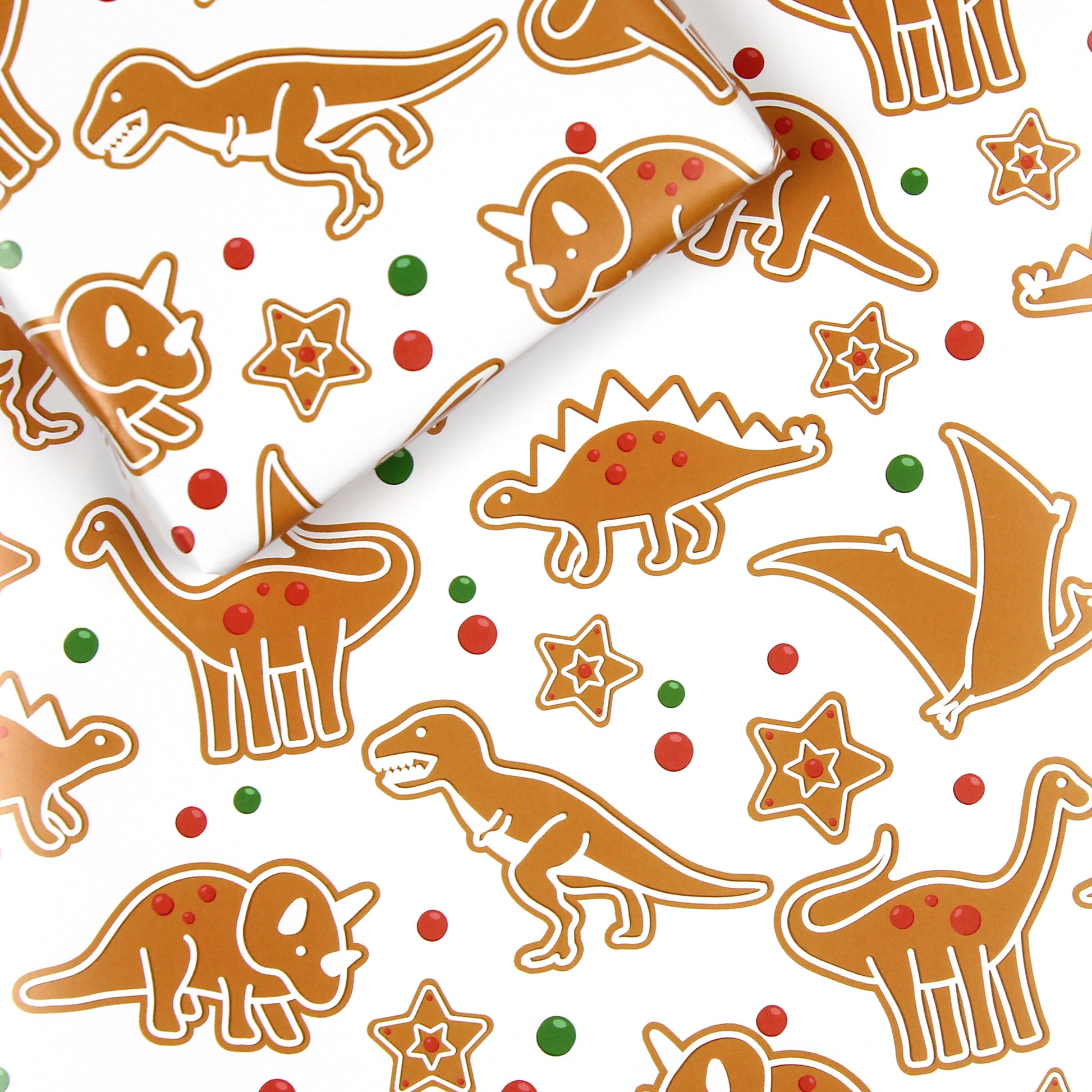 a sheet of gingerbread dinosaur wrapping paper with a box on top that is also wrapped in the same paper