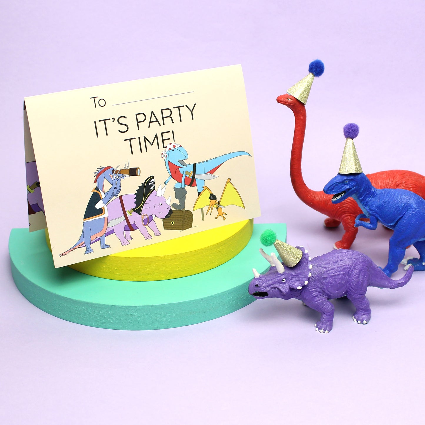 Pirate Dinosaur Invitation standing up on colourful wookden blocks with brightly coloured dinosaur figurines wearing party hats