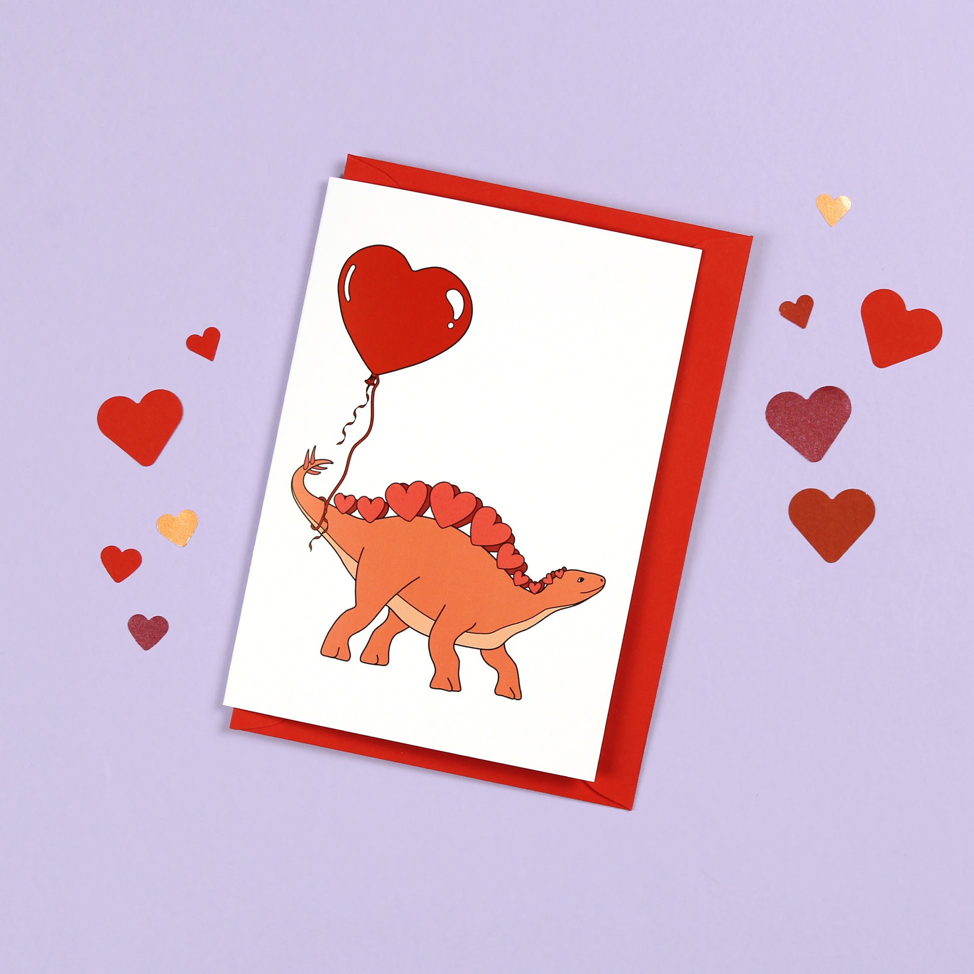 Heart Stegosaurus Dinosaur Greeting Card on a purple background with confetti hearts scattered around it
