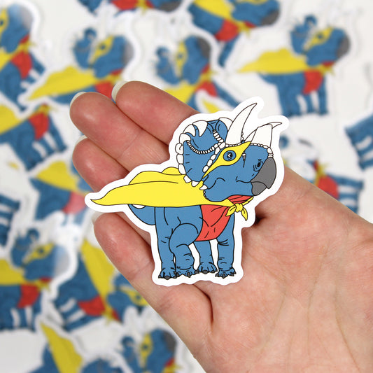 Superhero dinosaur sticker on a hand with out of focus stickers in the background.