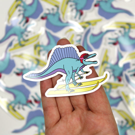 skiing dinosaur sticker on a hand with out of focus stickers in the background.