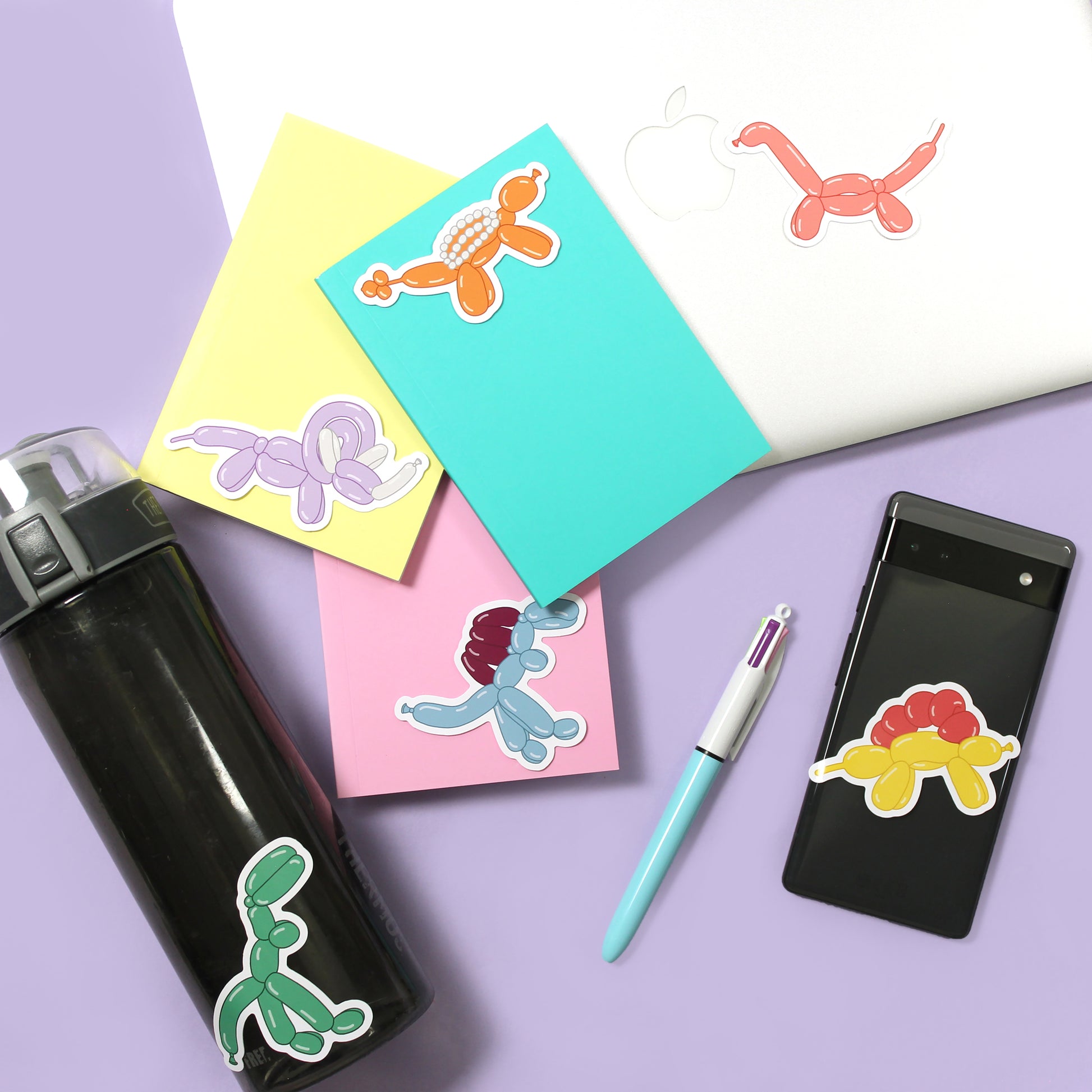 dinosaur balloon animal stickers on different items including a water bottle, notebooks, a laptop and back of a phone.