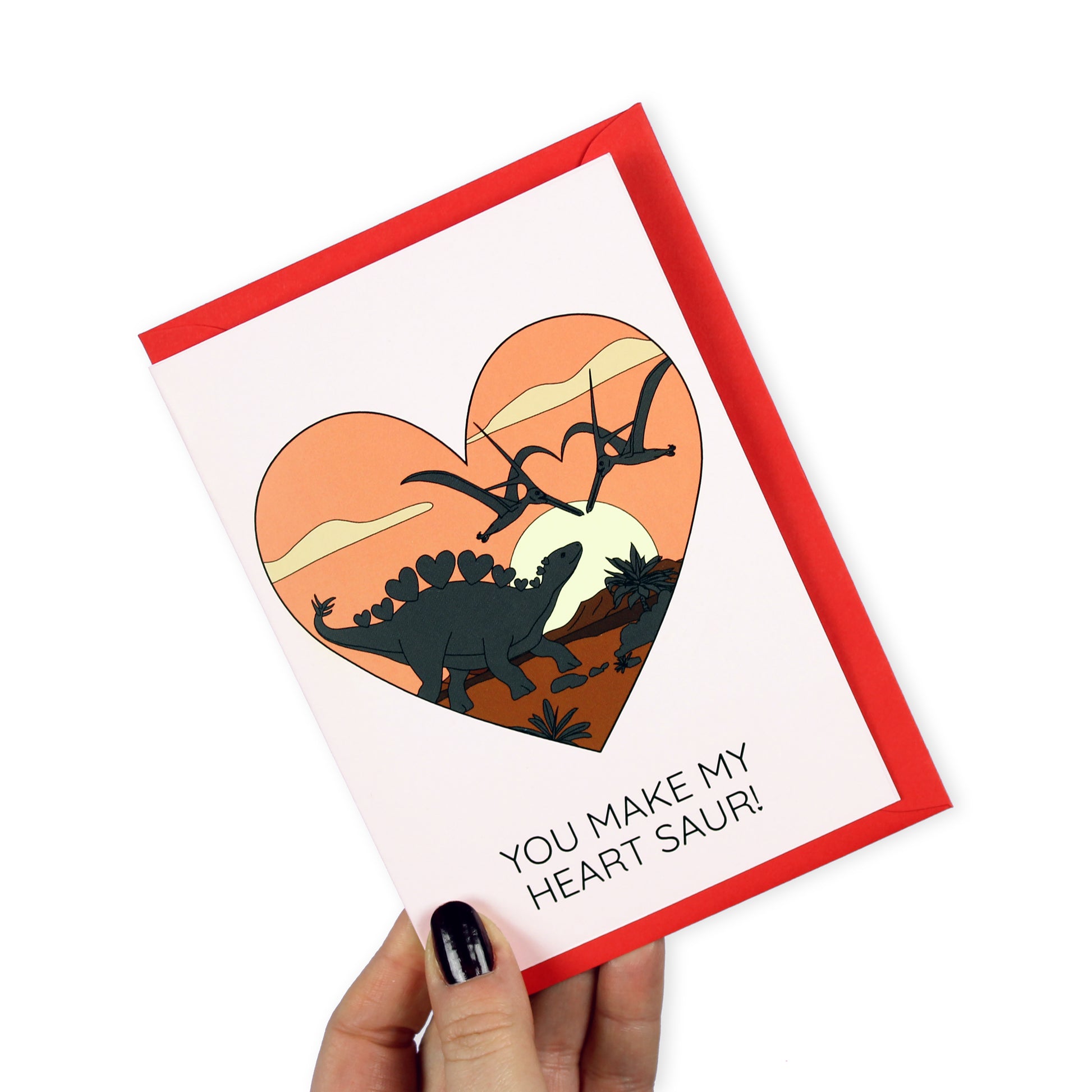 You make my heart saur dinosaur card held by a hand on a white background.