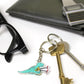 grabby arms t-rex dinosaur keyring on a split ring with keys. There is a pair of glasses, wallet and watch in the background