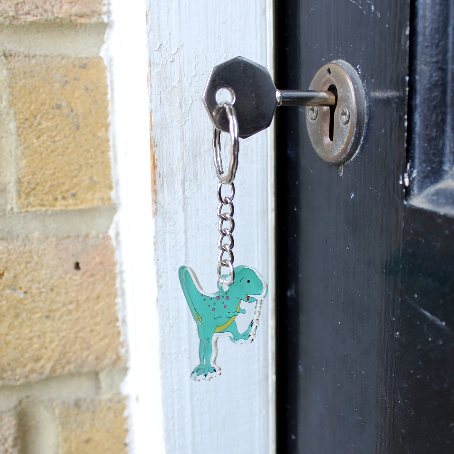 Zombie T-Rex dinosaur keyring hanging from a key which in in a lock on a door