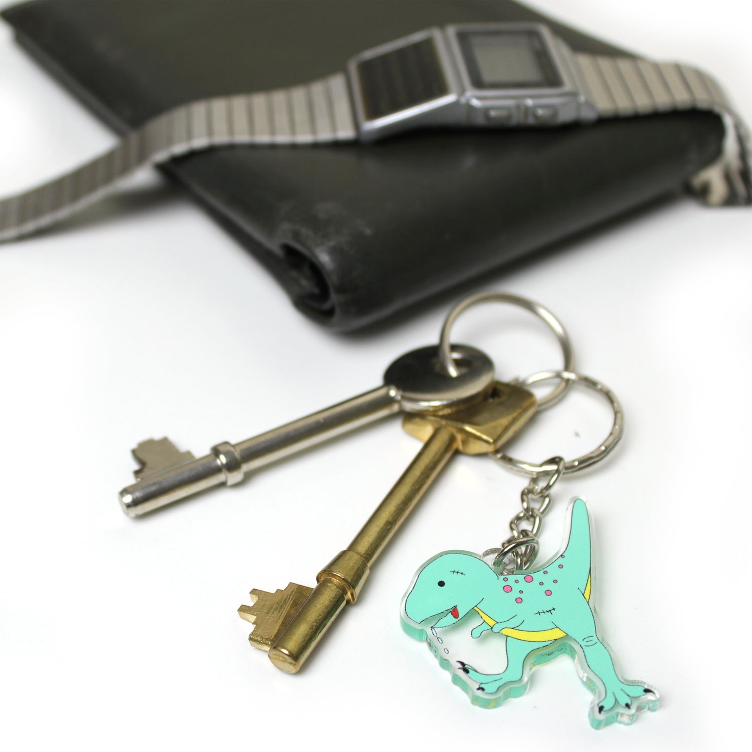 Zombie T-Rex dinosaur keyring on a split ring with keys. There is a leather wallet and watch in the background