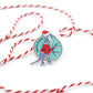 a Santa Claws acrylic pin on a white background with red and white stripe string around it