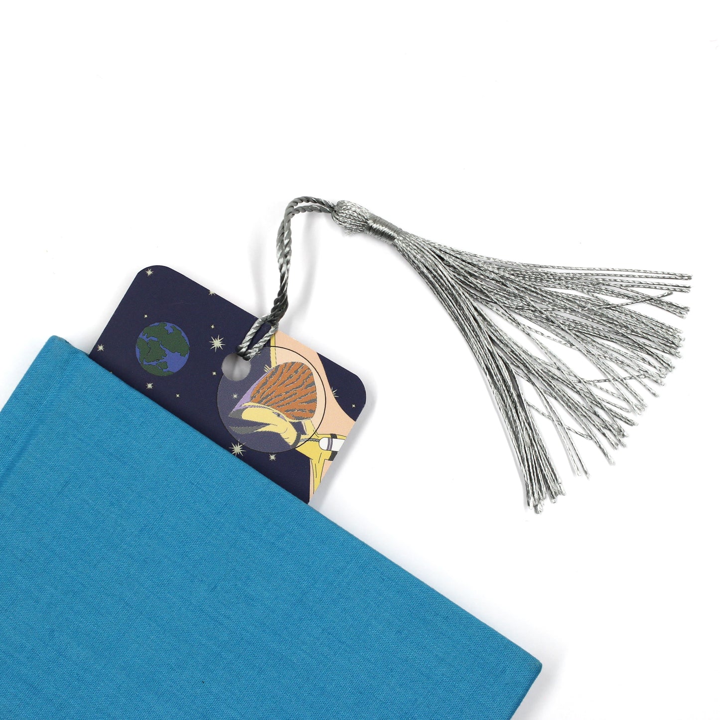 space dinosaur bookmark with a grey tassel coming out of a blue book