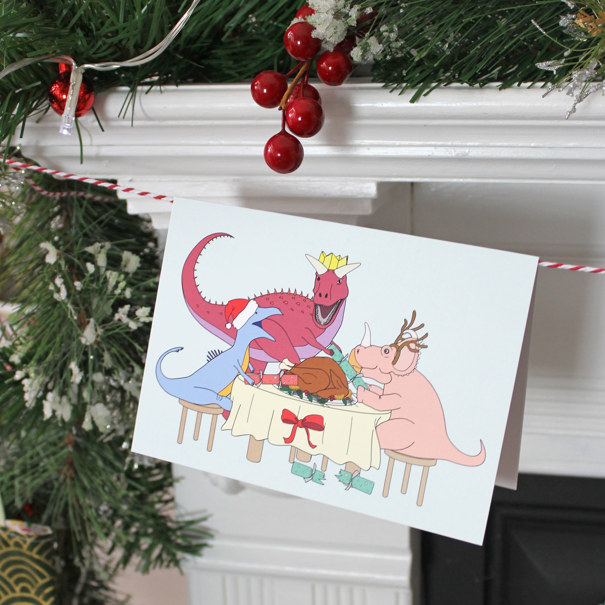 Dinner Dinosaur Christmas Greeting Card hanging from twine on a fireplace