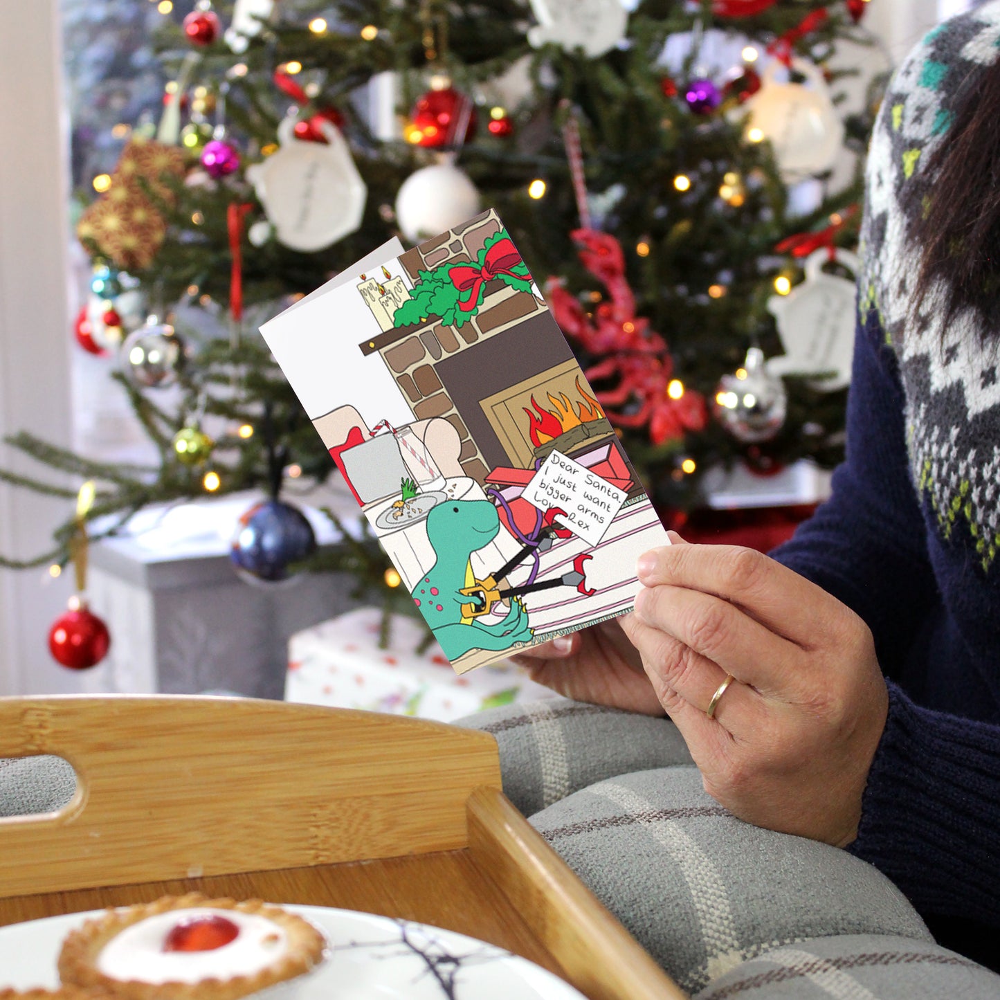 Christmas morning dinosaur card being held in front of a Christmas tree