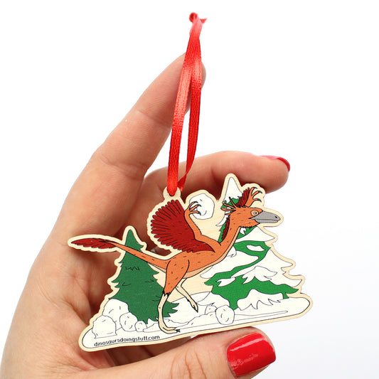 Hand holding a wooden Christmas decoration featuring a dinosaur throwing snowballs 