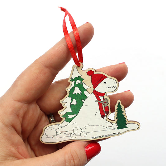 hand holding a wooden Christmas decoration with a t-rex snowman on it