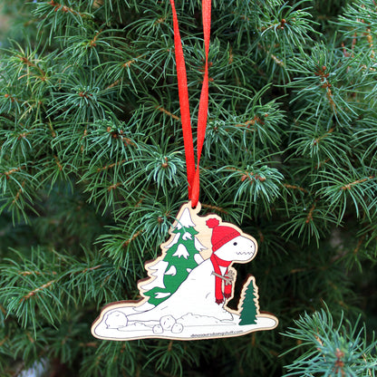 A wooden Christmas decoration with a t-rex snowman on it hanging from a Christmas tree