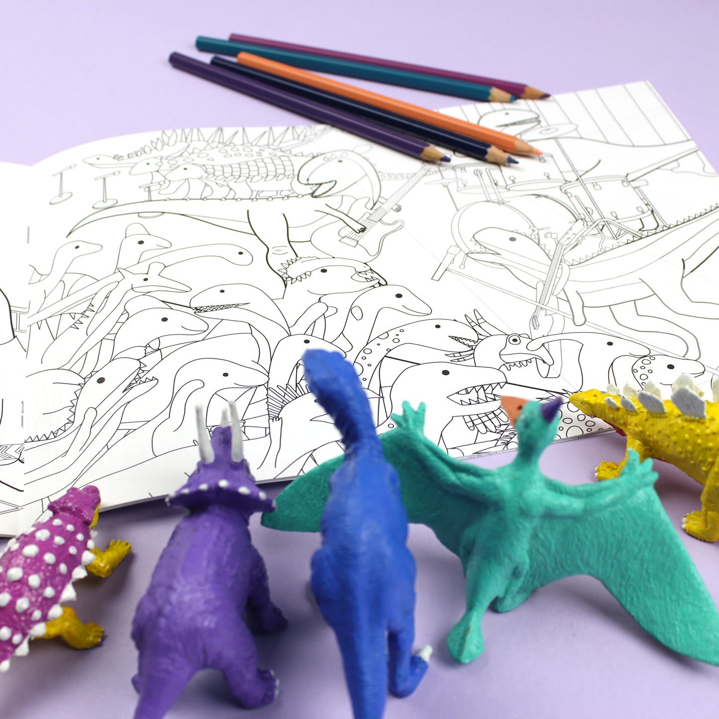 Inside page of Dinosaurs Doing Stuff colouring book. The page features black line illustrations of dinosaurs at a rock concert. A group of dinosaurs are crowding the stage while dinosaurs sing and play guitars.