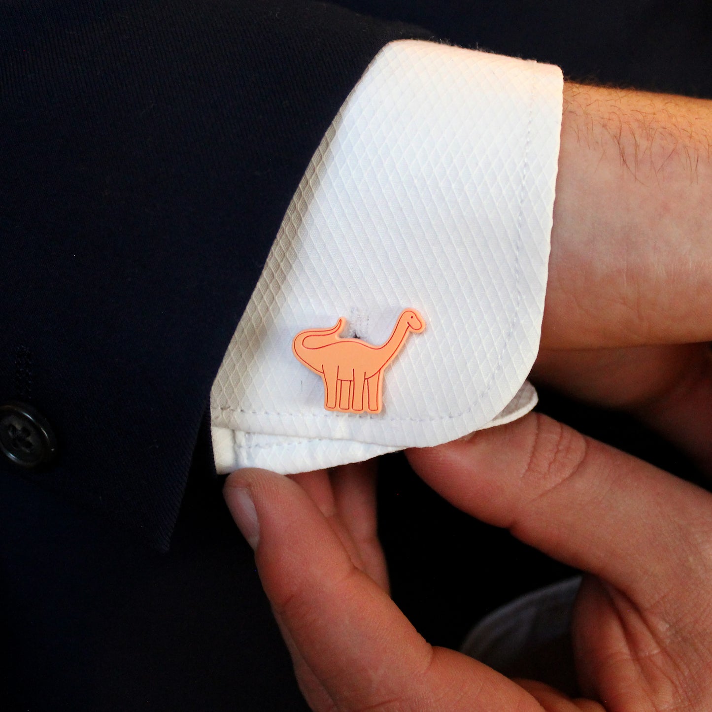 an orange brontosaurus cufflink on a white shirt being held by a hand