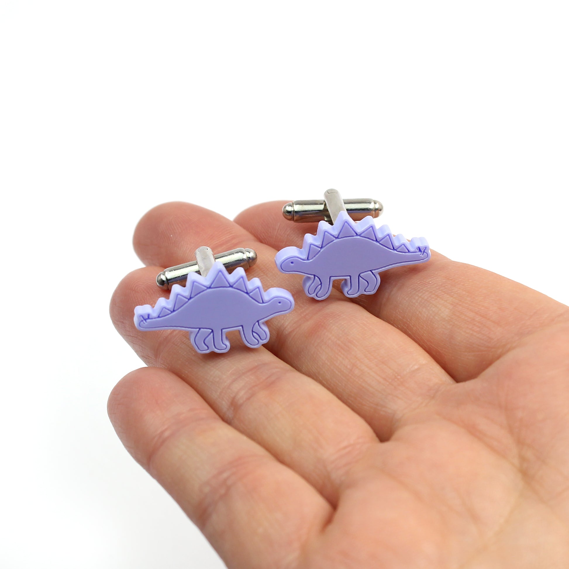 a pair of purple stegosaurus cufflinks on a hand