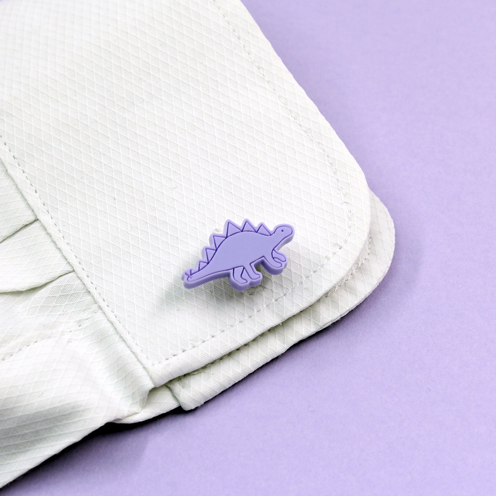 a purple stegosaurus cufflink on a white shirt cuff