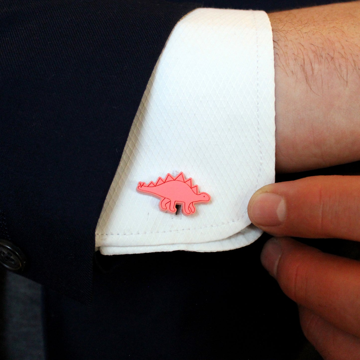 a red stegosaurus cufflink on a white shirt being held by a hand