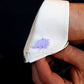 a purple triceratops cufflink on a white shirt being held by a hand