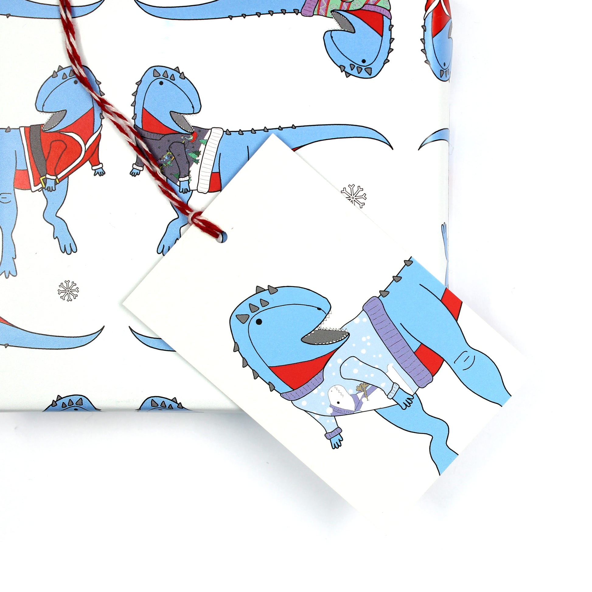 Ugly Christmas jumper dinosaur gift tag sitting on a box covered with matching wrapping paper