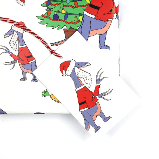 Santa claws dinosaur gift tag sitting on a box covered with matching wrapping paper