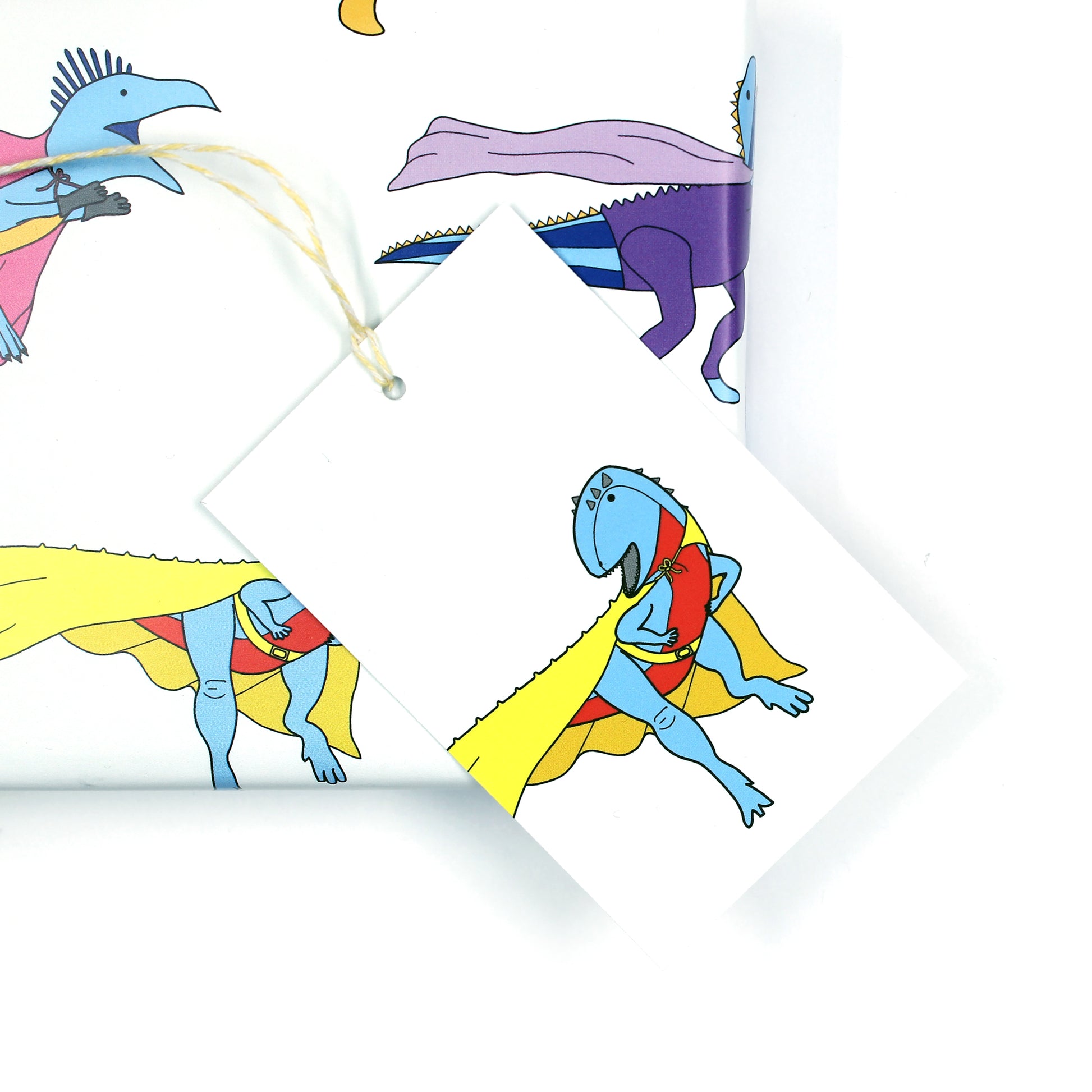 Superhero dinosaur gift tag sitting on a box covered with matching wrapping paper