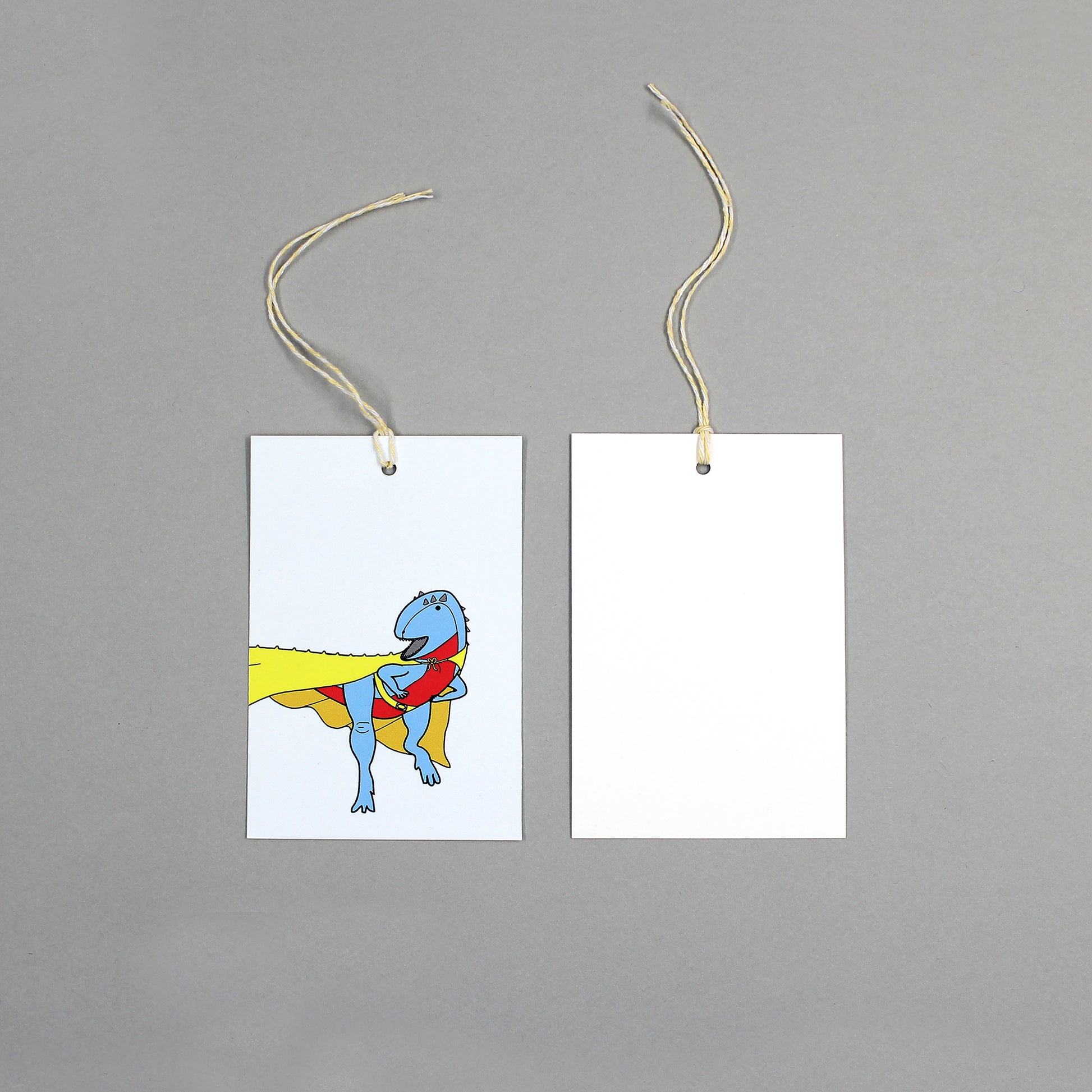 flat lay showing the front and back of the superhero dinosaur gift tag on a grey background