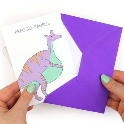 hands holding an envelope while removing the preggo-saurus dinosaur card from the envelope
