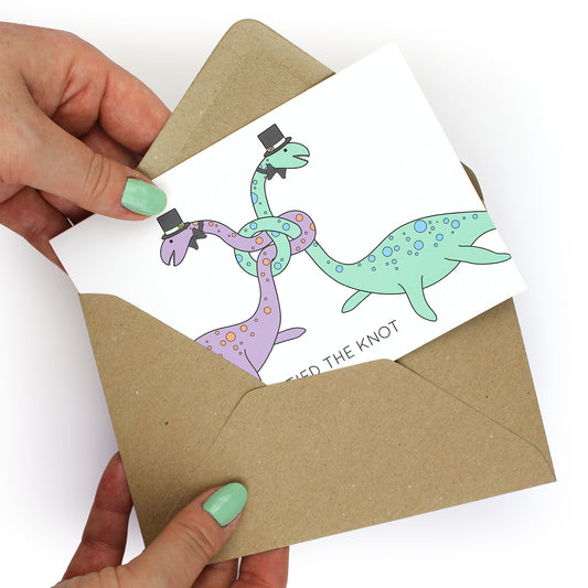 hands holding an envelope while removing the tied the knot dinosaur card from the envelope