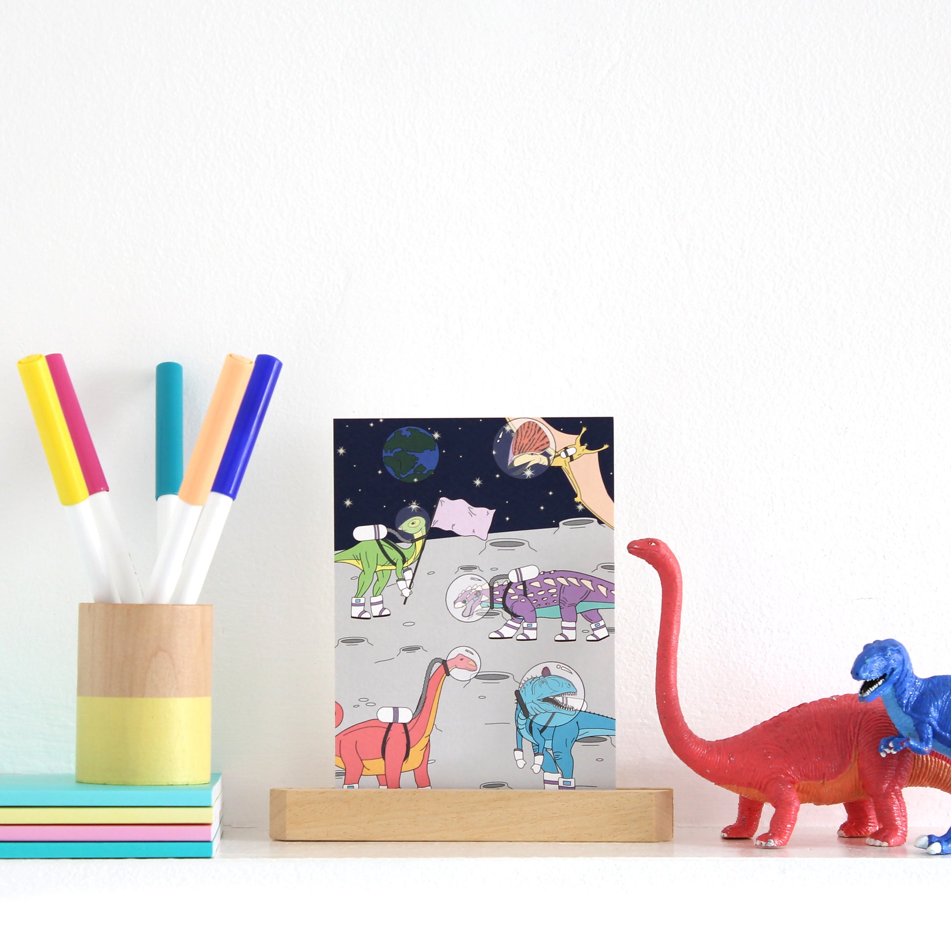 space dinosaur postcard displayed in a wooden stand on a shelf