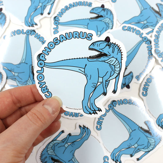 Titanoceratops dinosaur sticker held by a hand with scattered stickers behind it