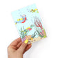 hand holding an under the sea dinosaur postcard