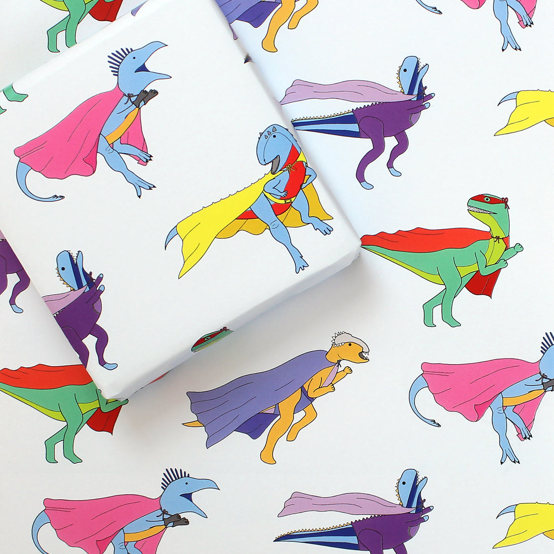 a sheet of superhero dinosaur wrapping paper with a box on top that is also wrapped in the same paper