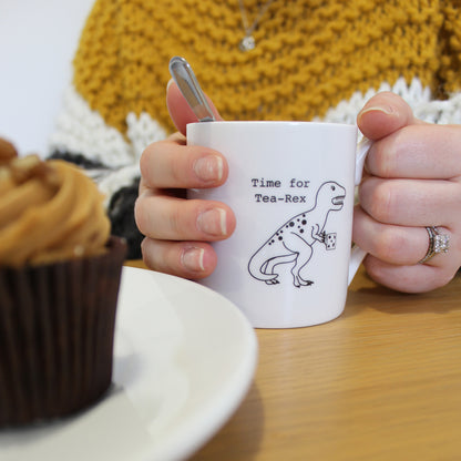 Hands holding a Time for Tea-Rex Mug with a cupcake next to it