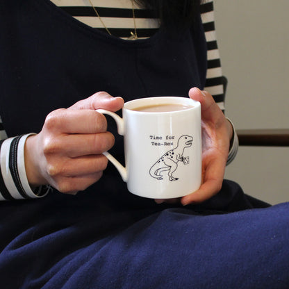 Time for Tea-Rex Mug held by a person in a navy jumpsuit and stripe top